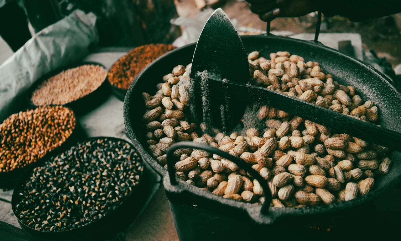 Close-up of raw peanuts in a pan surrounded by various grains in bowls.