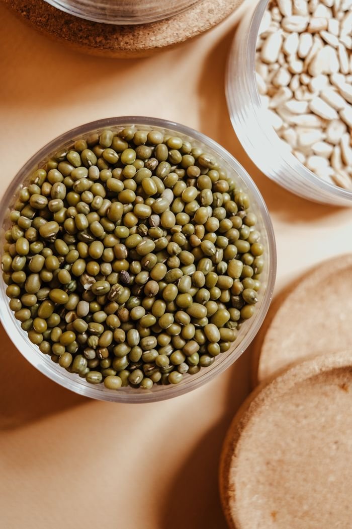 Top view of organic mung beans and seeds in glass jars, showcasing natural food storage.