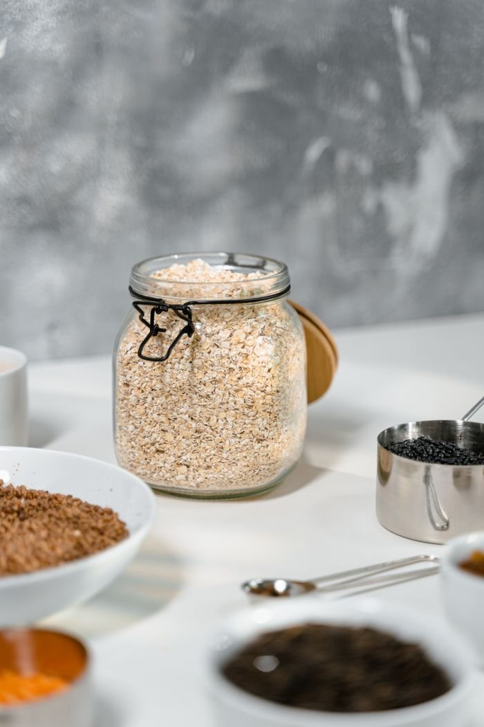 A collection of dried breakfast grains in a jar with bowls and cups on a white table.